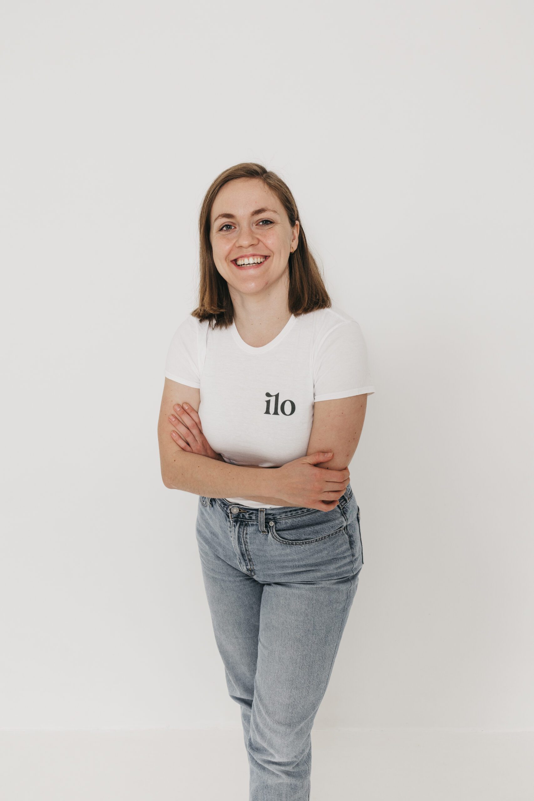 Smiling person in a white ilo t-shirt and jeans against a white background.